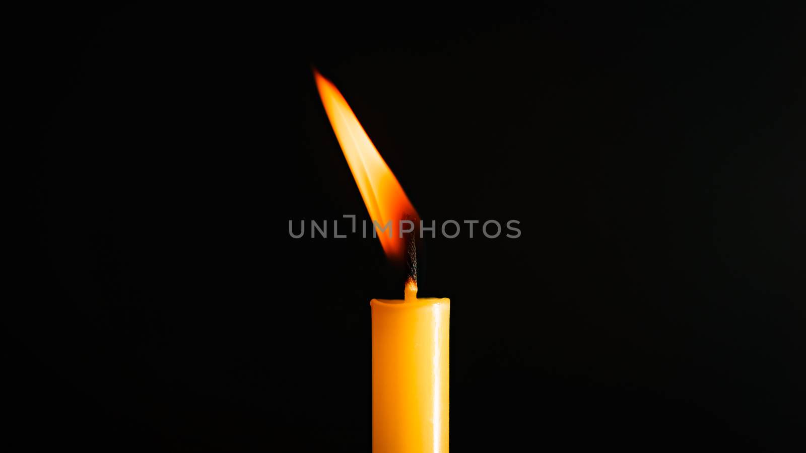 Close-up of a yellow candle illuminated in a black background.