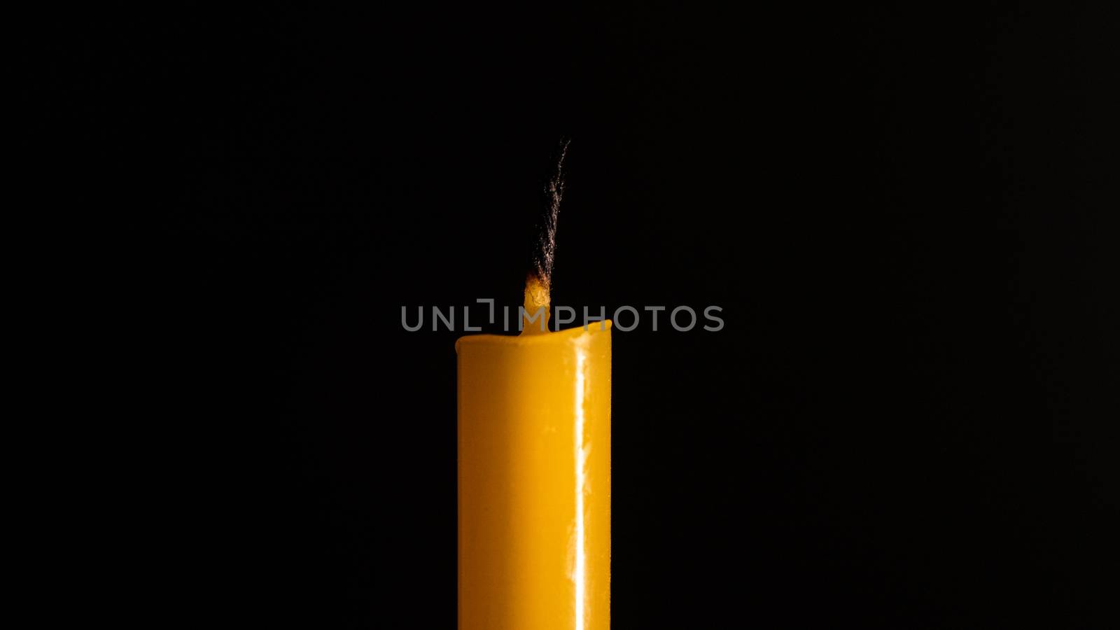 Close-up of a yellow candle illuminated in a black background. by ToonPhotoClub