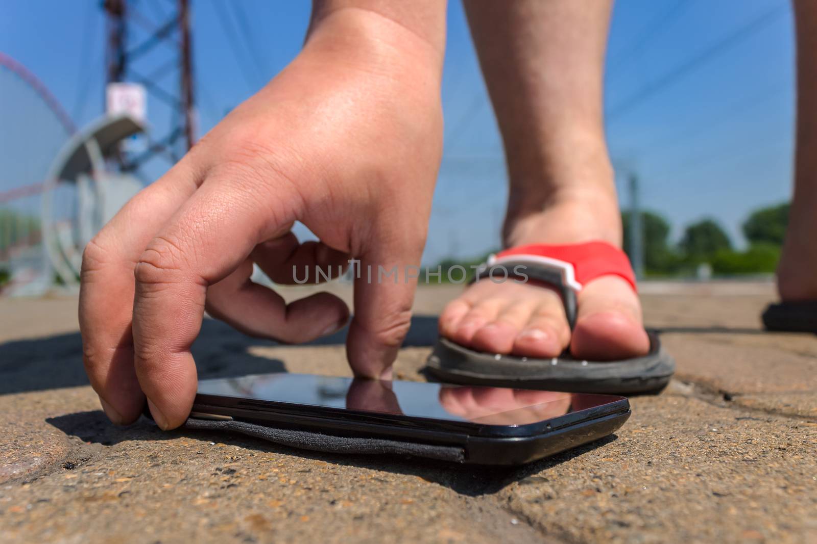 A man picks up a mobile phone that fell on the road in a public park in the summer