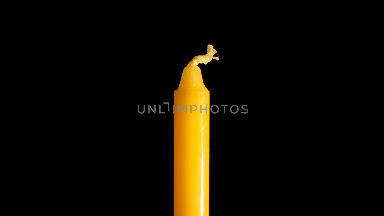 A close up of a yellow candle in a black background