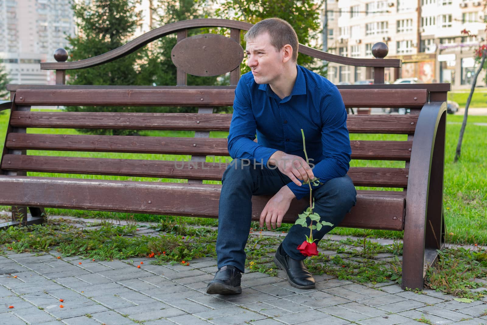 Displeased man with a rose in his hands is watching someone in the park by Skaron
