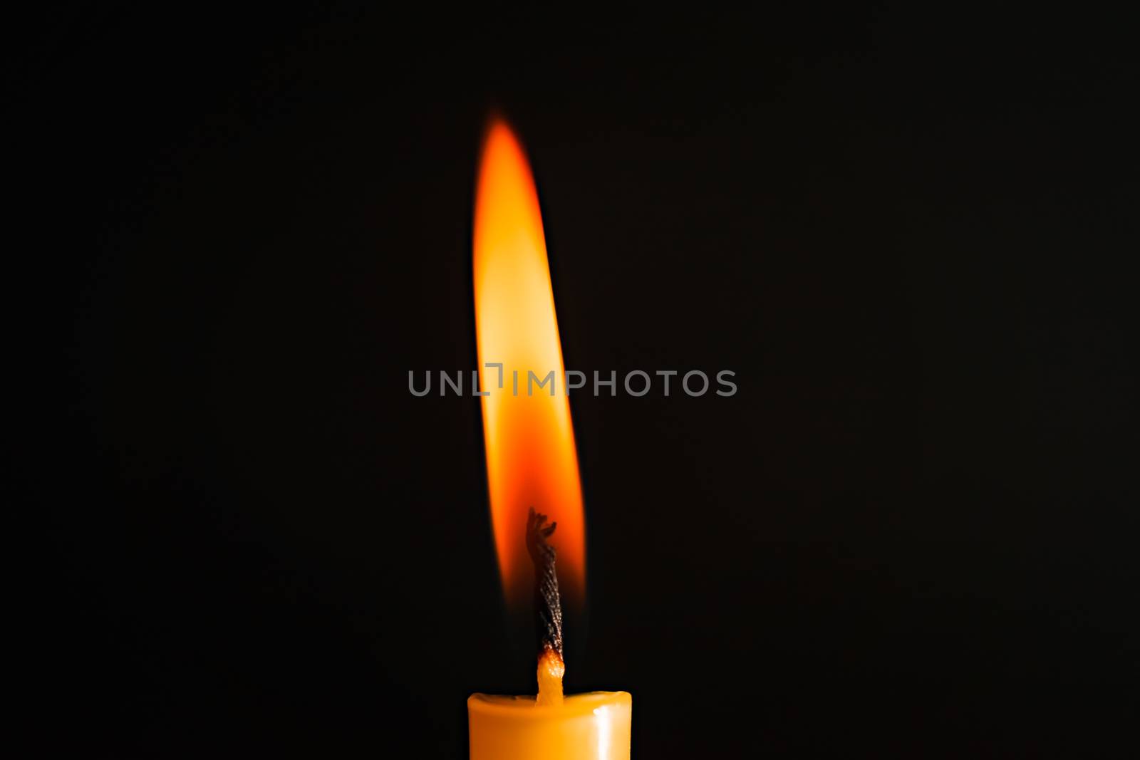 Close-up of a yellow candle illuminated in a black background. by ToonPhotoClub