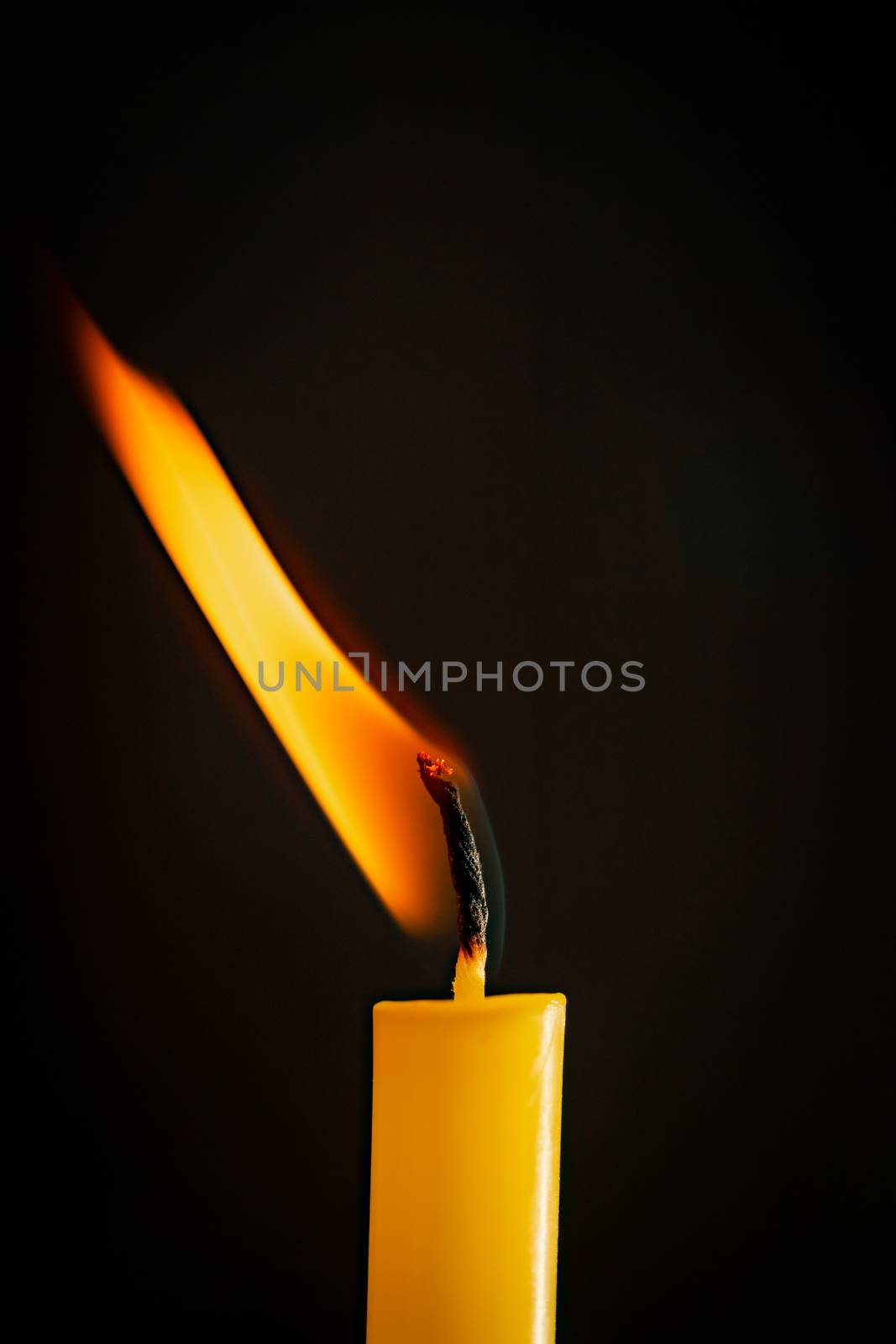 Close-up of a yellow candle illuminated in a black background. by ToonPhotoClub