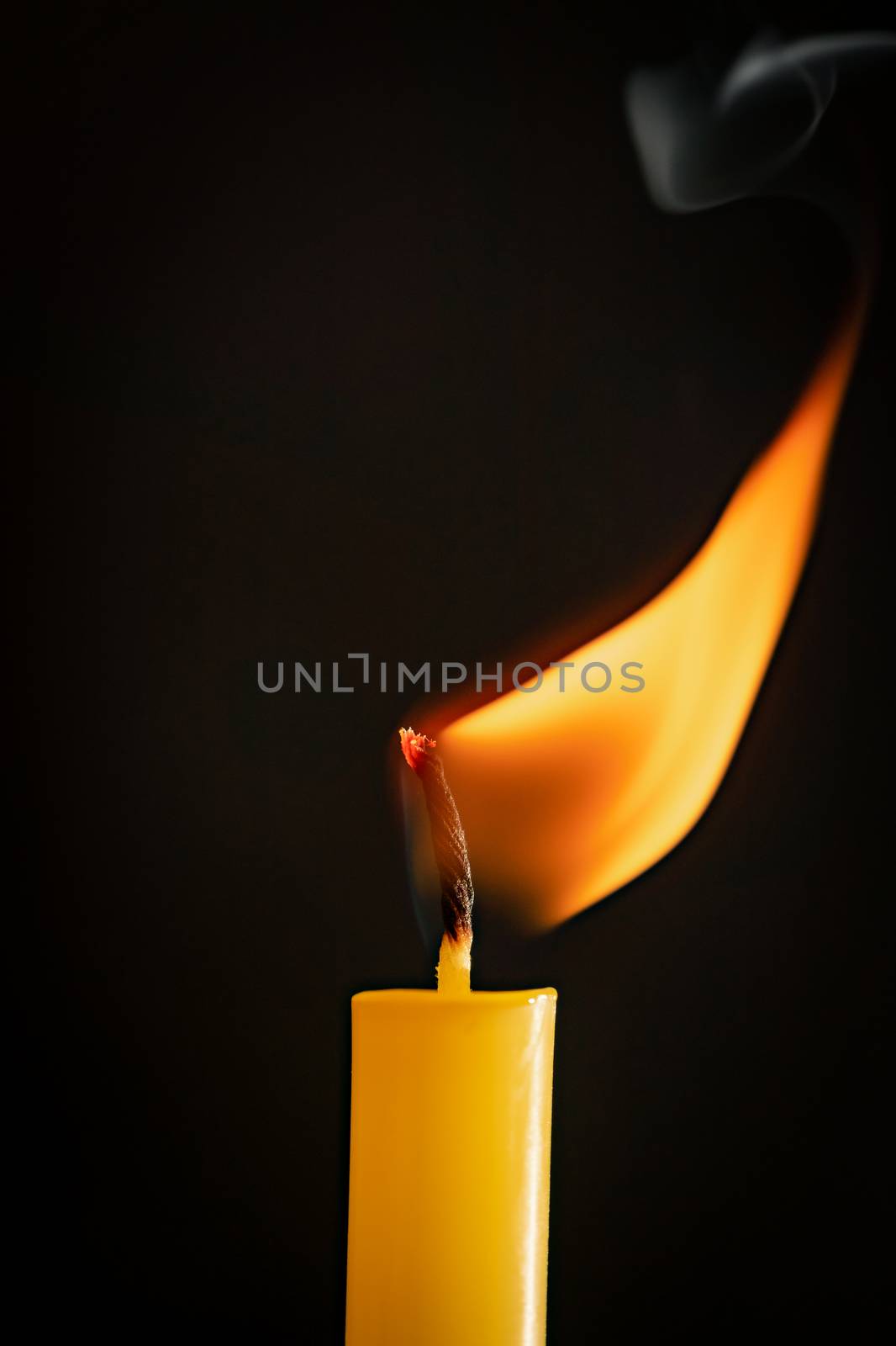 Close-up of a yellow candle illuminated in a black background. by ToonPhotoClub