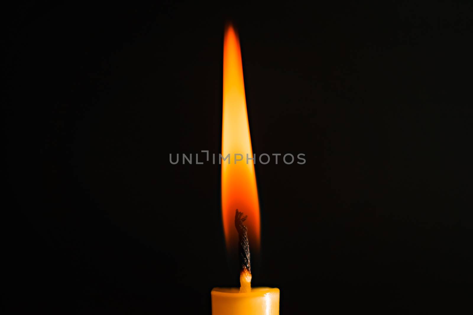 Close-up of a yellow candle illuminated in a black background.