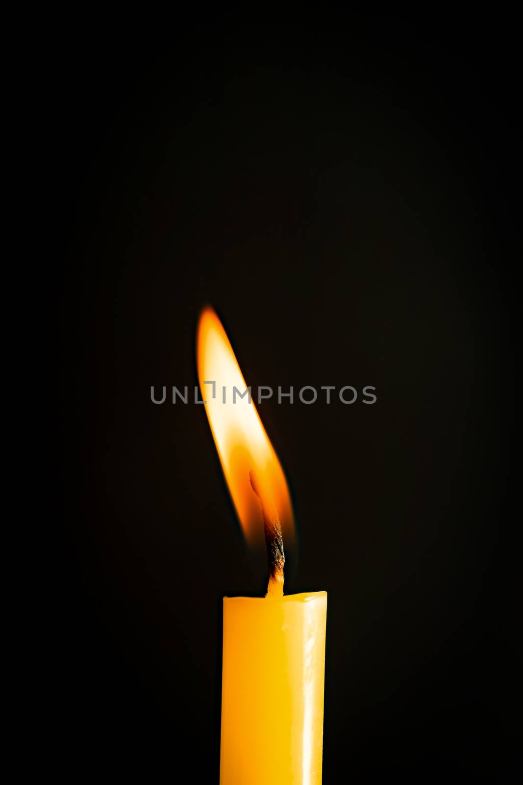 Close-up of a yellow candle illuminated in a black background.