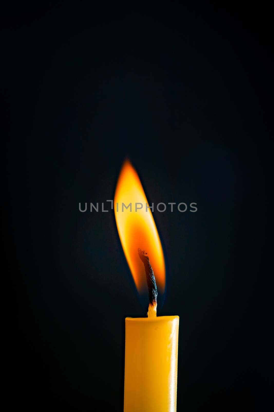 Close-up of a yellow candle illuminated in a black background. by ToonPhotoClub