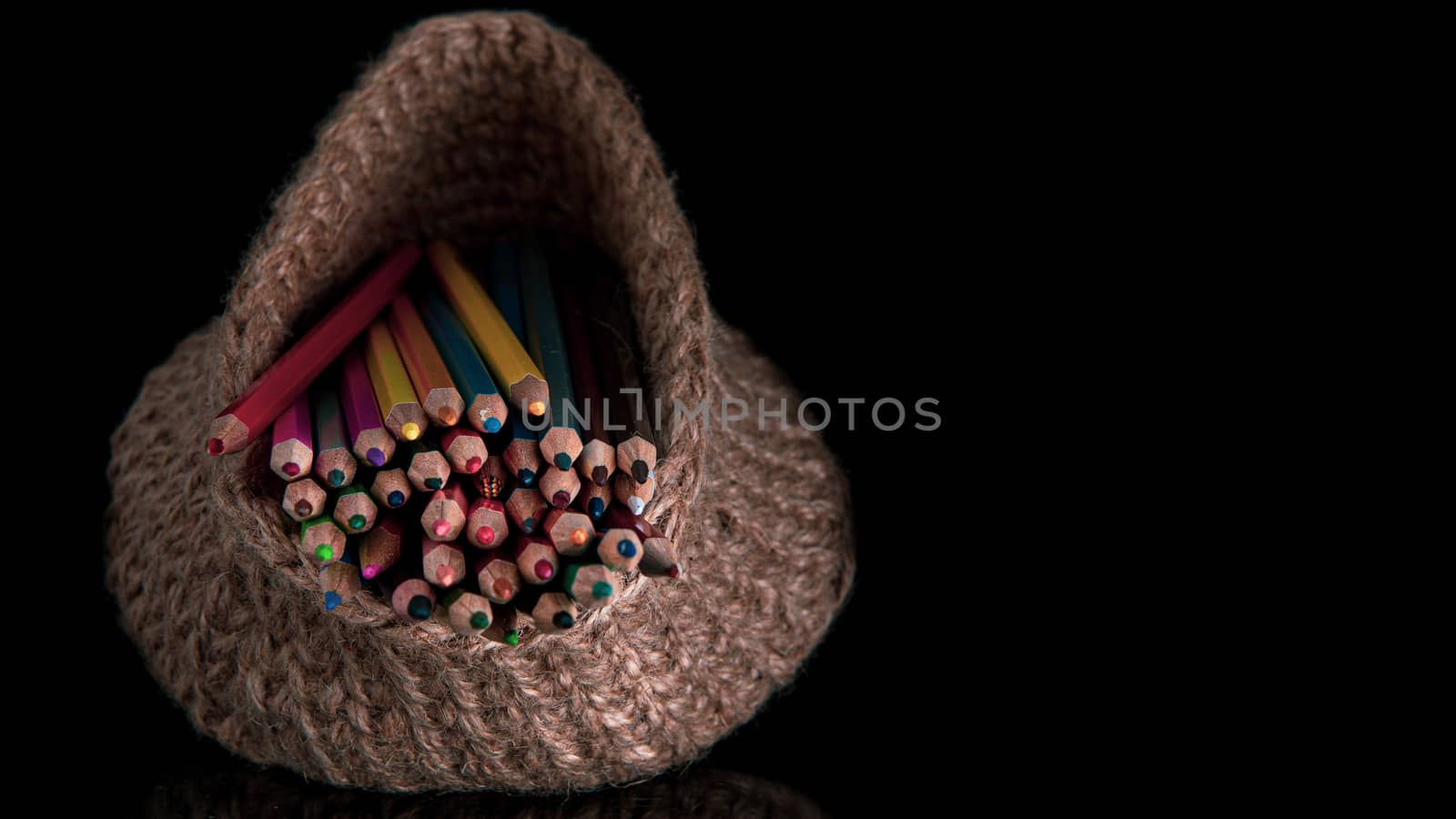 colored pencils in a knitted basket on a black background by marynkin