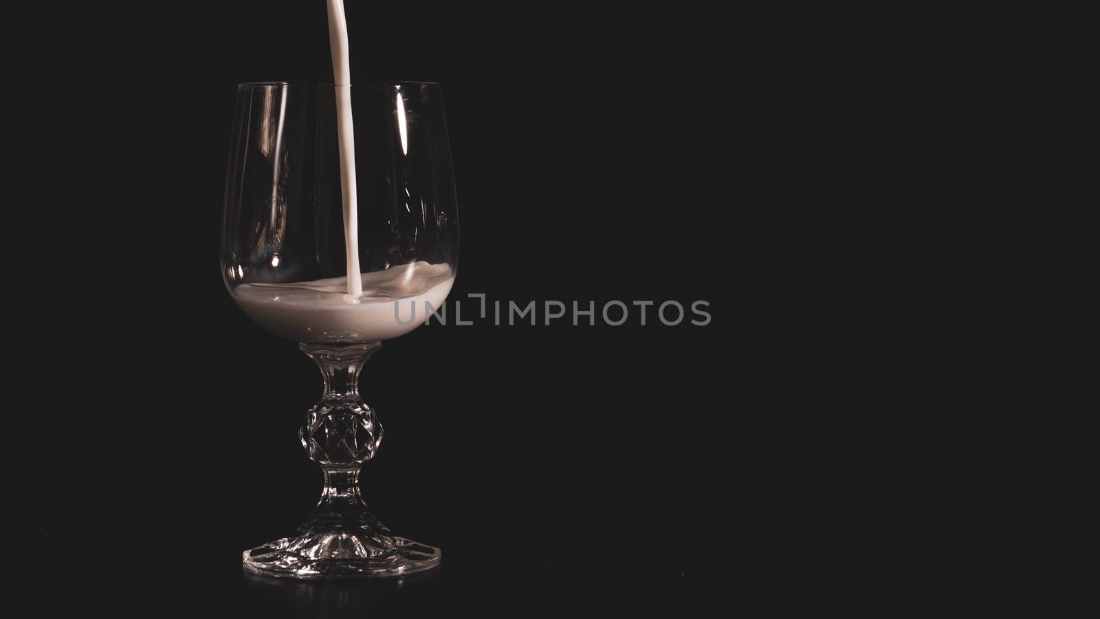 A transparent glass for wine is filled with milk on a black background by marynkin