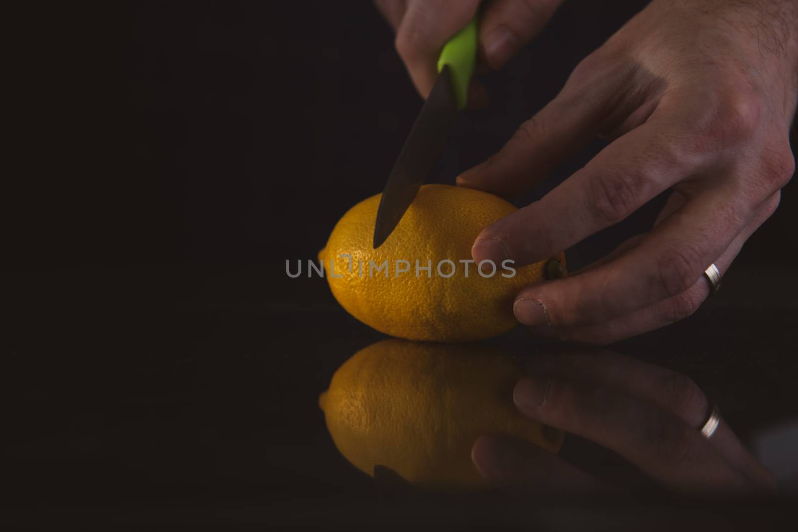 Man's hand cuts lemon with knife on black background with copy space