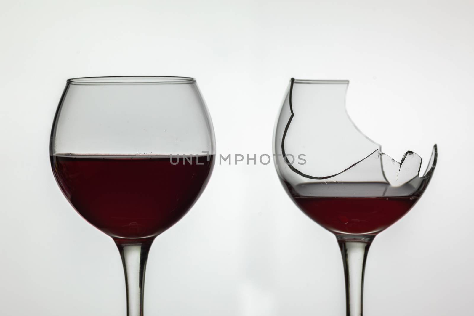 Broken and not broken wine glass with red wine on white background.