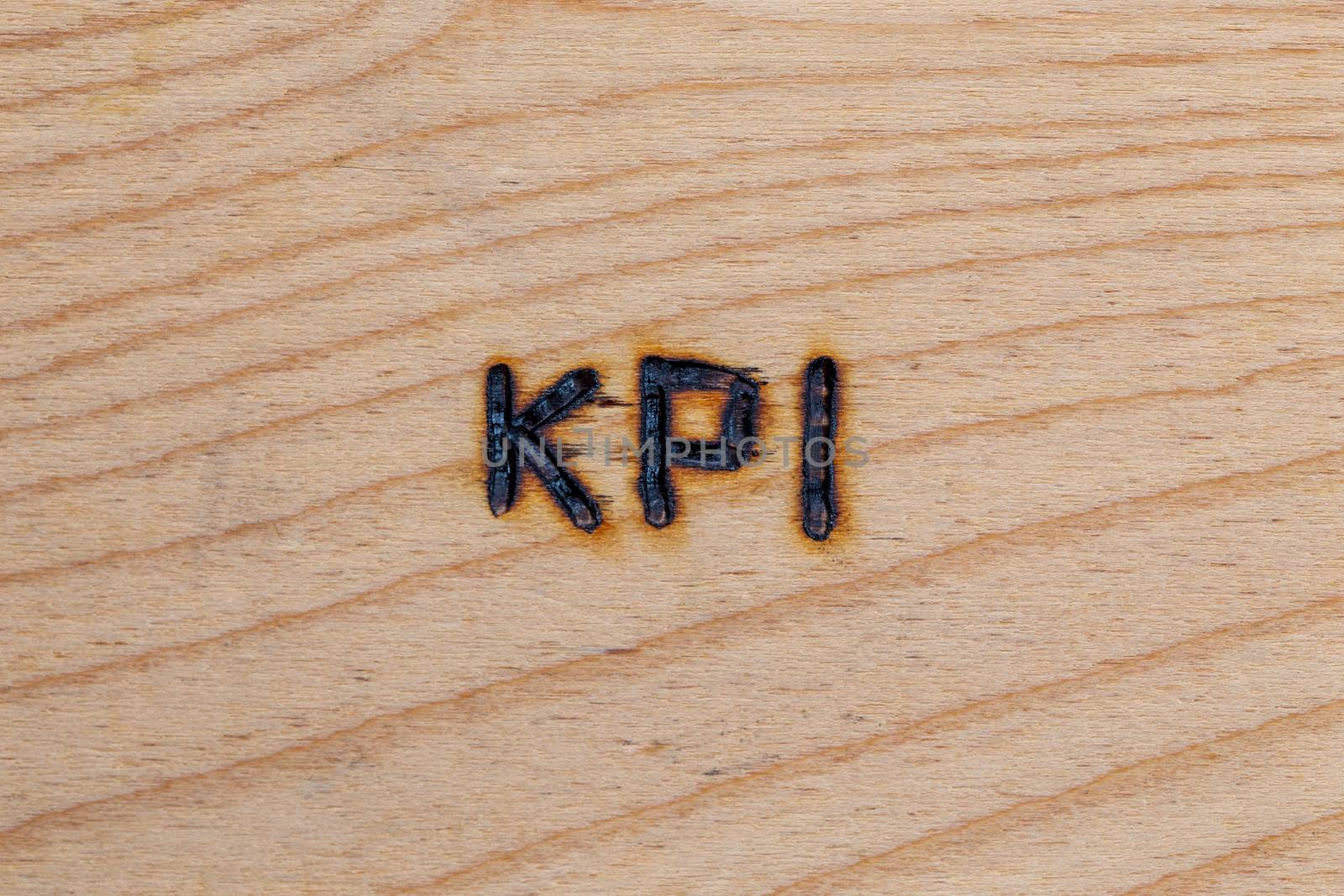 an abbreviation KPI - key performance indicator - burned by hand with electric wood burner on plywood surface.
