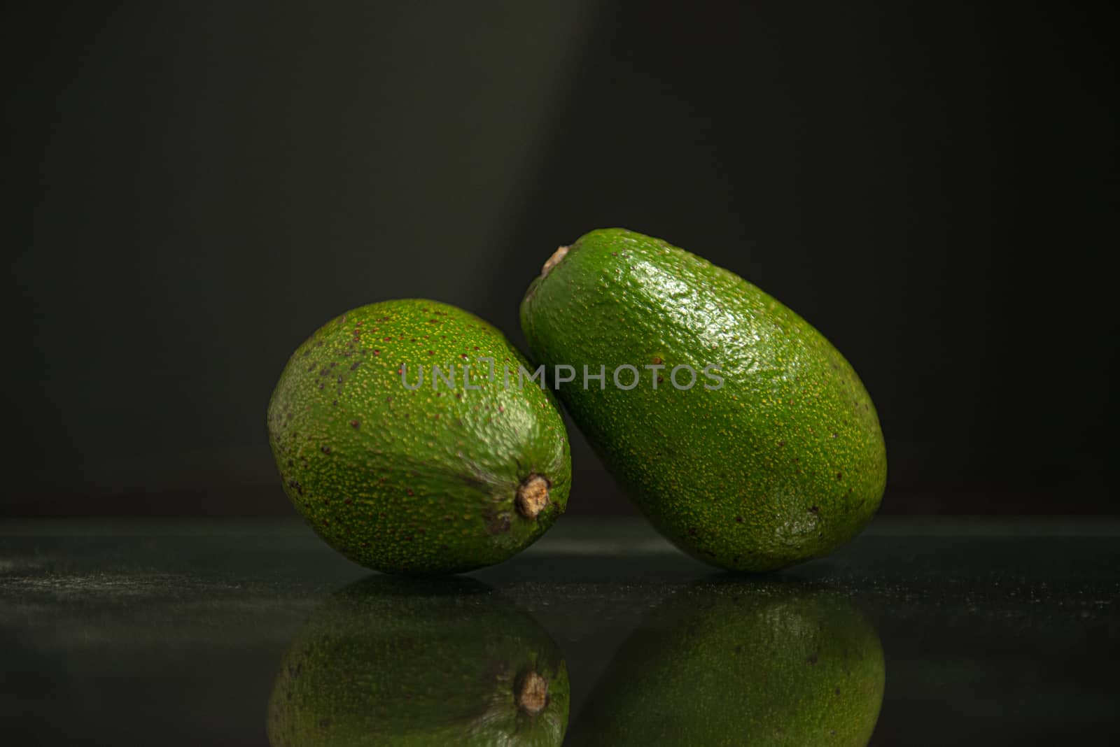 two whole avocados with reflection and copy space on a black background by marynkin