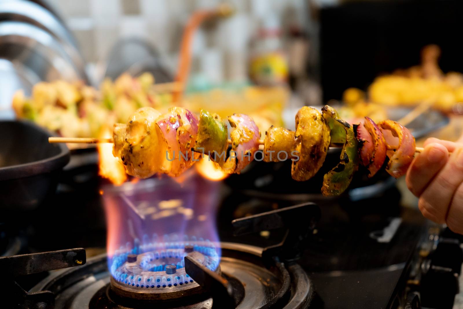 Macro selective focus shot of cottage cheese, onions, mushrooms and more on a wooden skewer roasted over an open flame to char it. Shows home cooking of indian paneer tikka masala a tasty spicy street food with charred vegetables