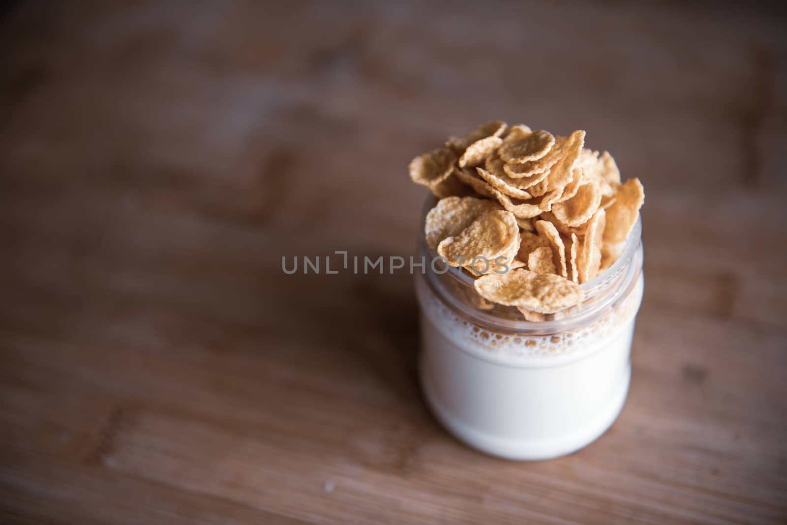 Delicious breakfast - glass jar of yogurt with cornflakes stands on a wooden table with copy space by marynkin