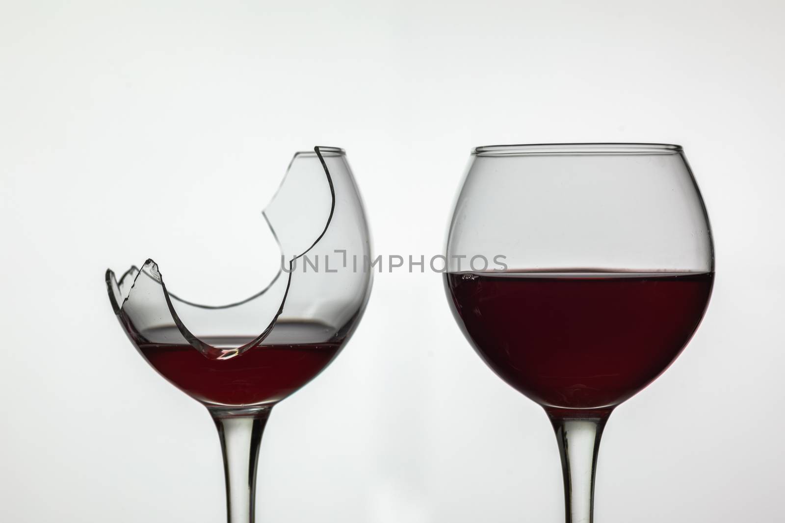 Broken and not broken wine glass with red wine on white background.