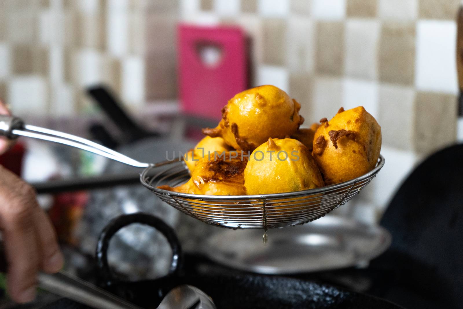 Shallow depth of feild shot of vada potatoes wrapped in flour being taken out of hot oil after deep frying by Shalinimathur