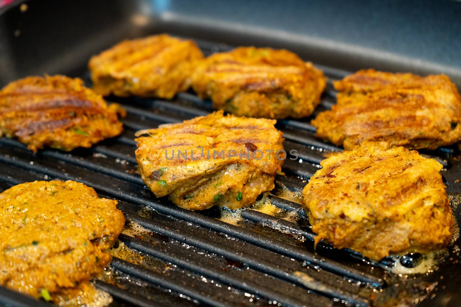 Shallow depth of feild shot mince meat mutton patties keema roasting on a pan with oil bubbling out as they get charred . Shows an easy hearty home meal with protein and barbeque.