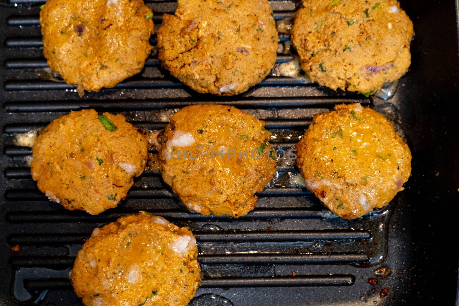 Shallow depth of feild shot mince meat mutton patties keema roasting on a pan with oil bubbling out as they get charred . Shows an easy hearty home meal with protein and barbeque.