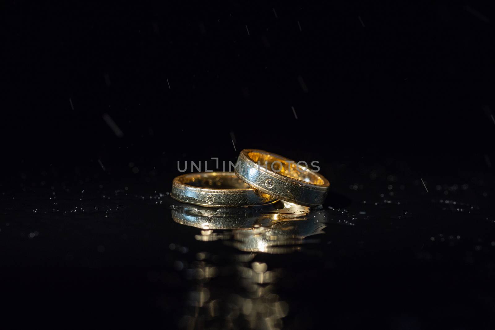 Wedding rings lying on dark surface shining with light close up macro. Water splashes