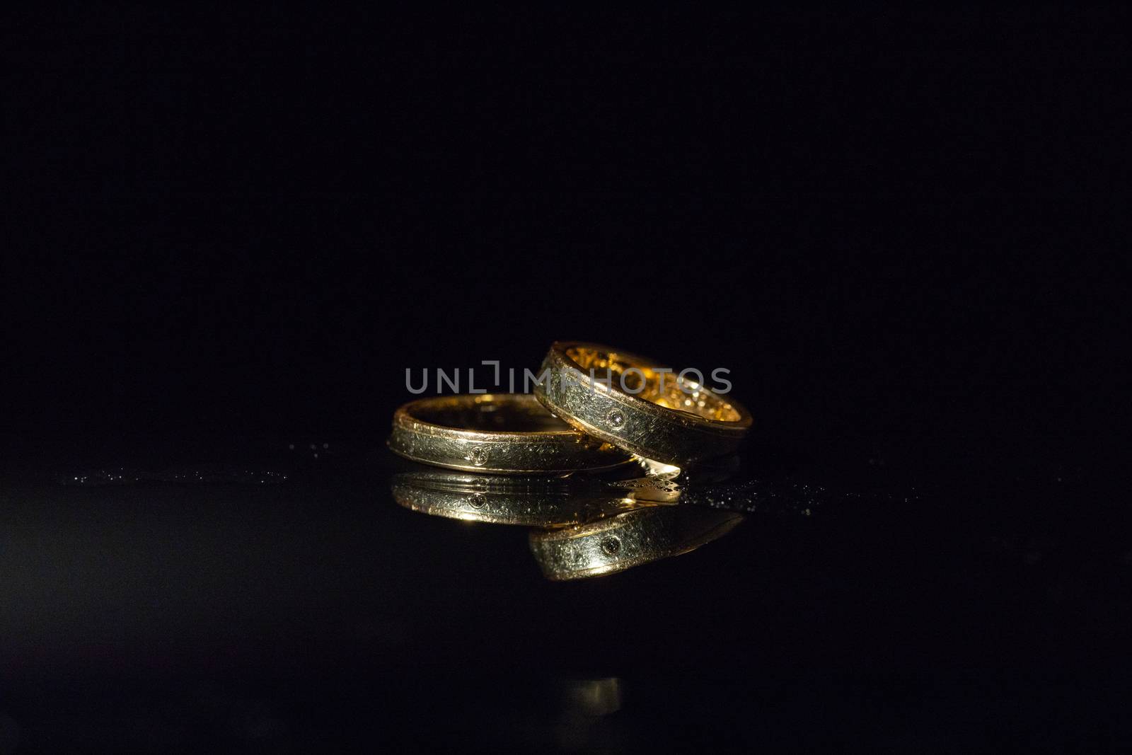 Wedding rings lying on dark surface shining with light close up macro. Water splashes