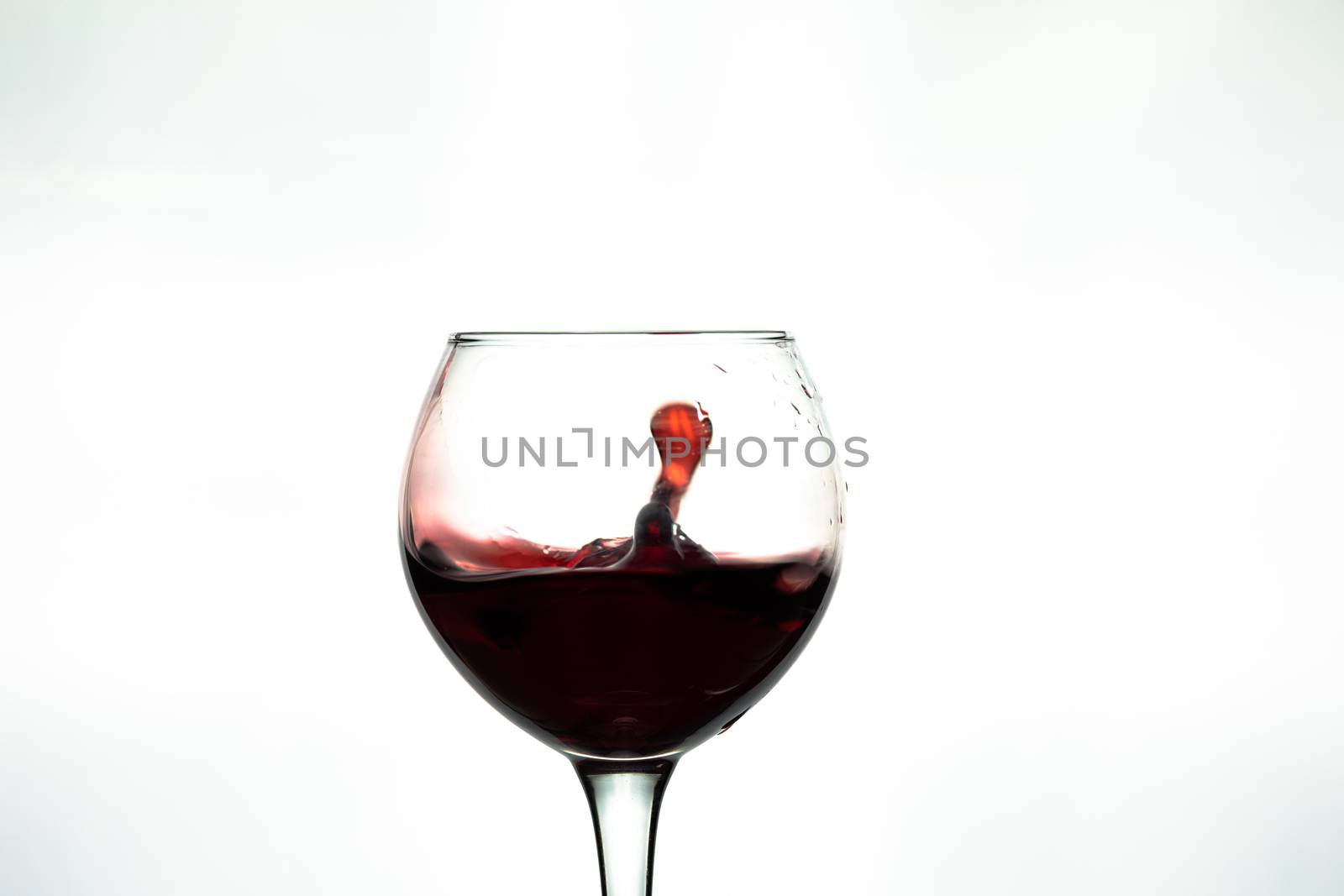 Red wine splash into glass on white background.