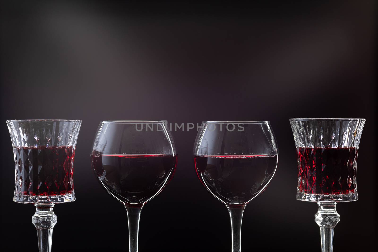 Rose wine. Red wine in four wine glasses over dark background with rays of light.