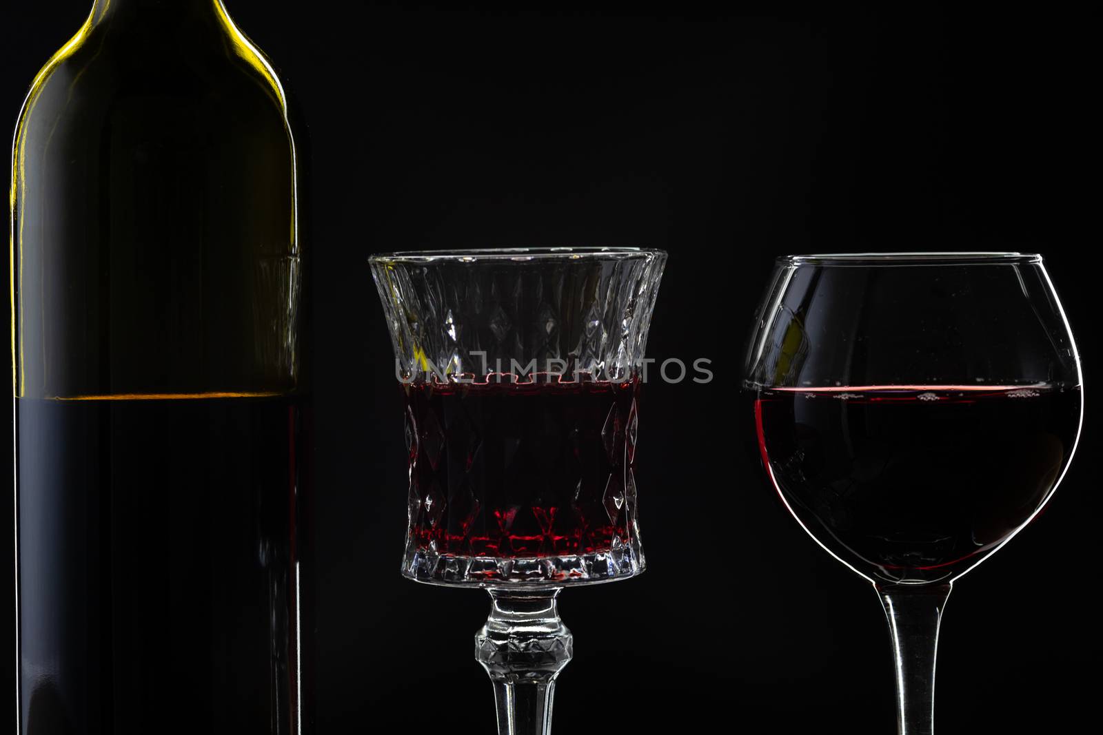 Wine. Red wine in two wine glasses over dark background. Silhouette of bottle with rose wine