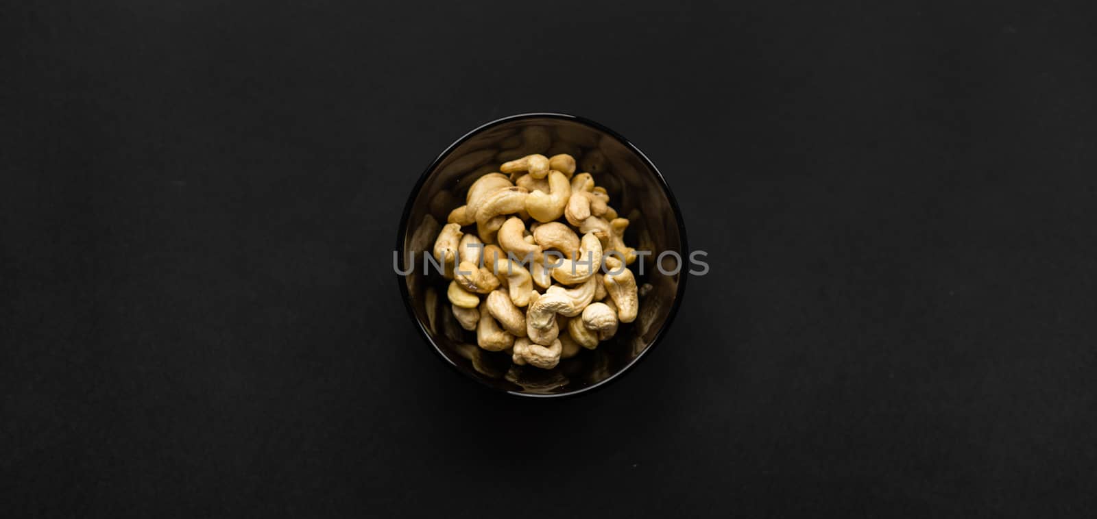 Cashew nuts in a small plate on a black table as a background. Cashew nut is a healthy vegetarian protein nutritious food. by vovsht