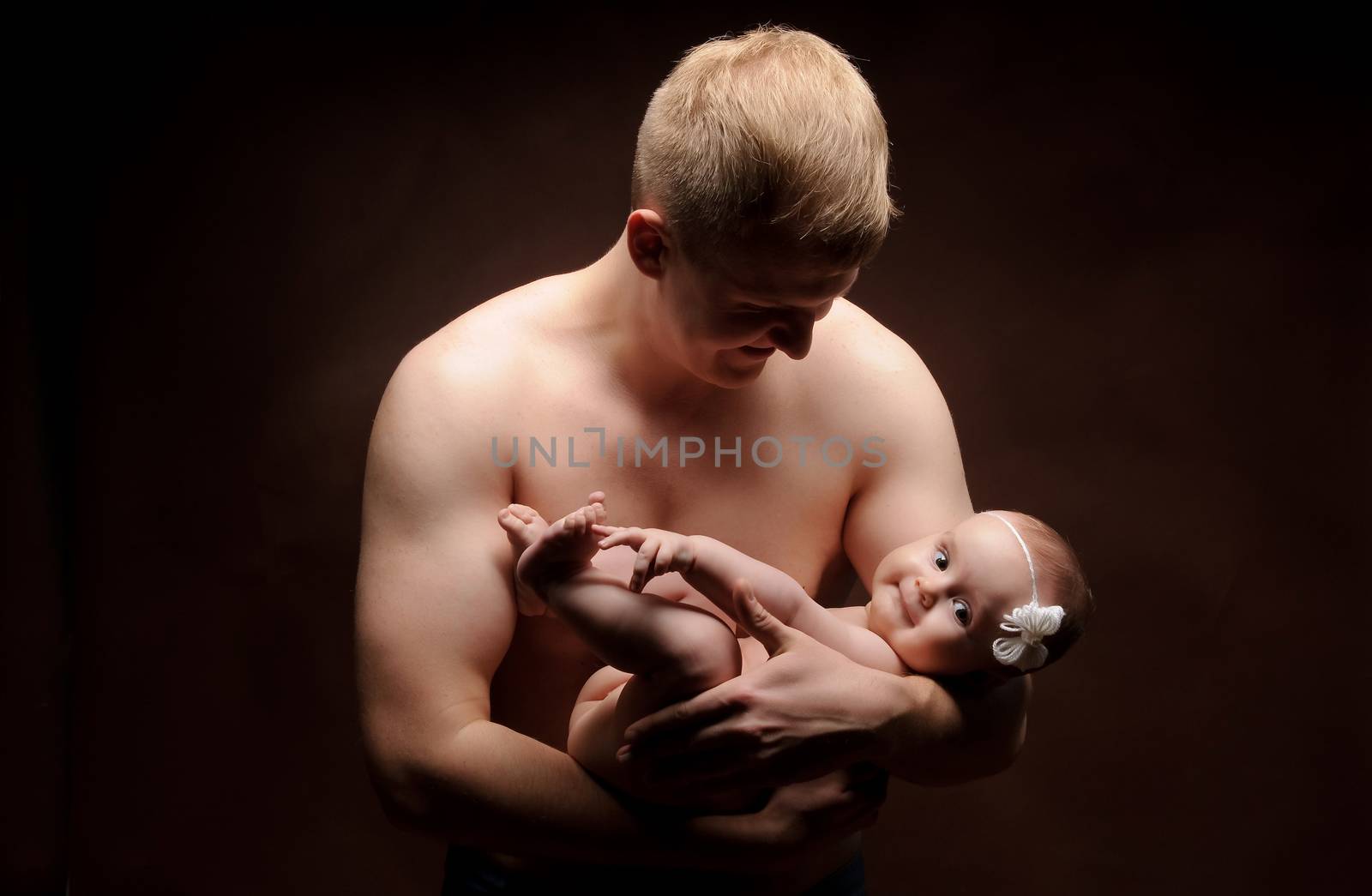 Male holding nice infant baby girl. Daughter on father's arms. Human growth and development. New generation. Cheerful man and his baby. New life concept. Dark background