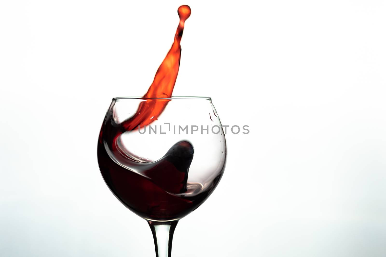 Red wine splash into glass on white background.