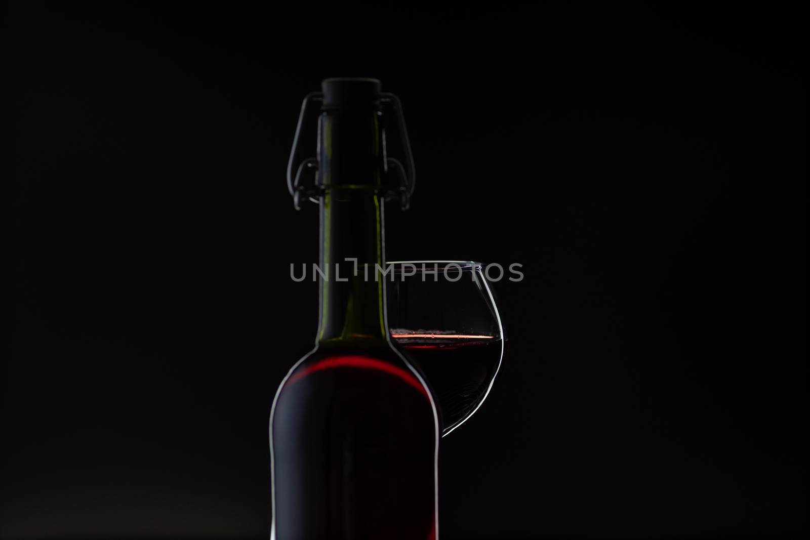 Wine. Red wine in wine glass over dark background. Silhouette of bottle with rose wine and opener on cork