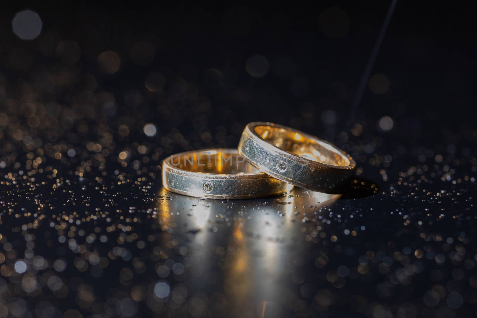 Wedding rings lying on dark surface shining with light close up macro. Water splashes