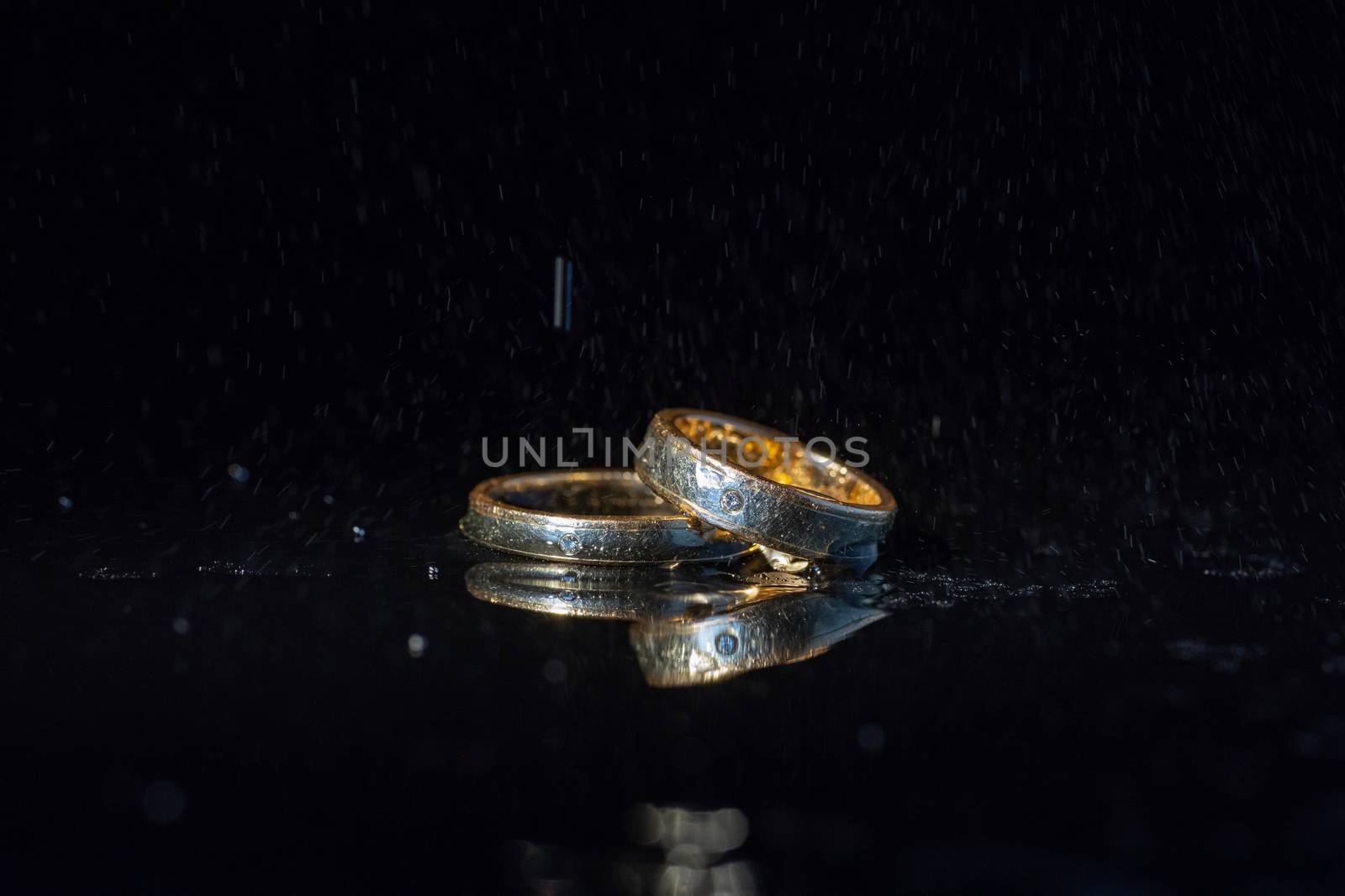 Wedding rings lying on dark surface shining with light close up macro. Water splashes