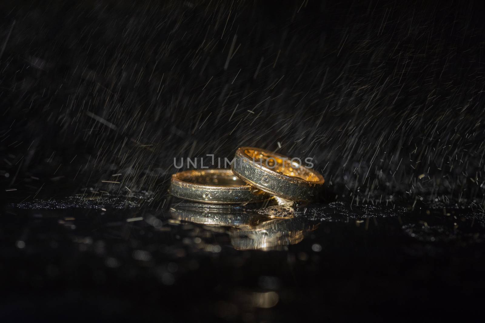 Wedding rings lying on dark surface shining with light close up macro. Water splashes