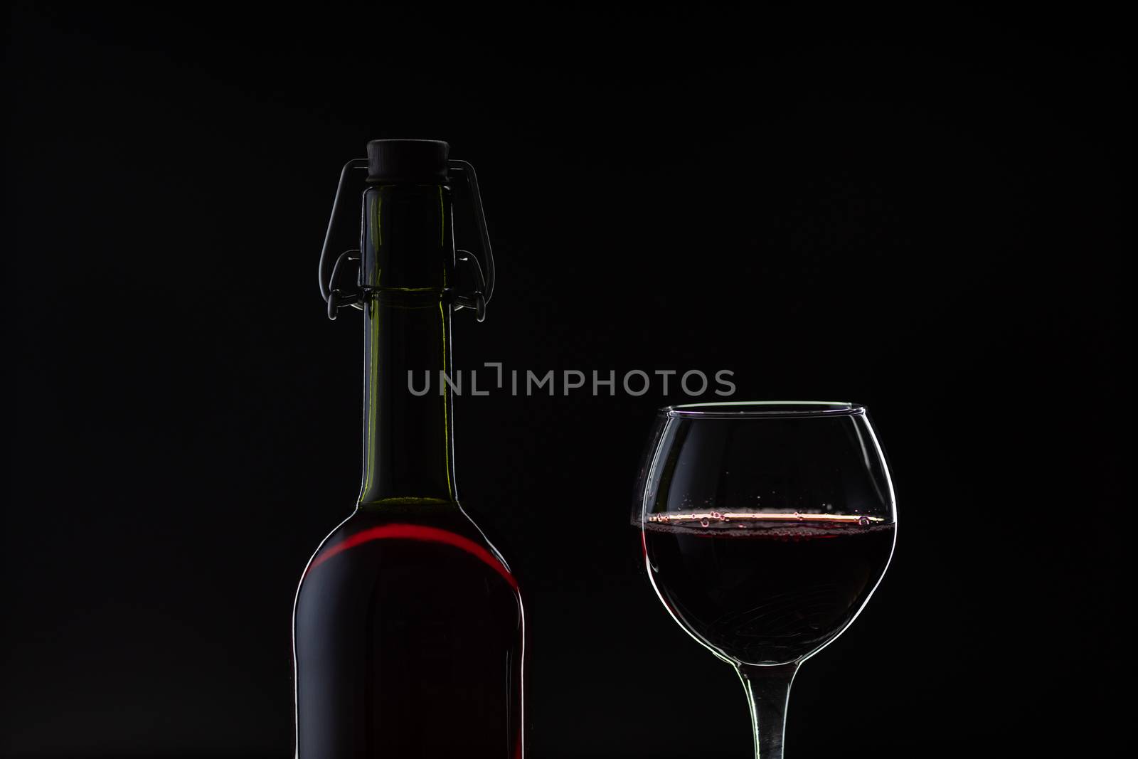 Wine. Red wine in wine glass over dark background. Silhouette of bottle with rose wine and opener on cork