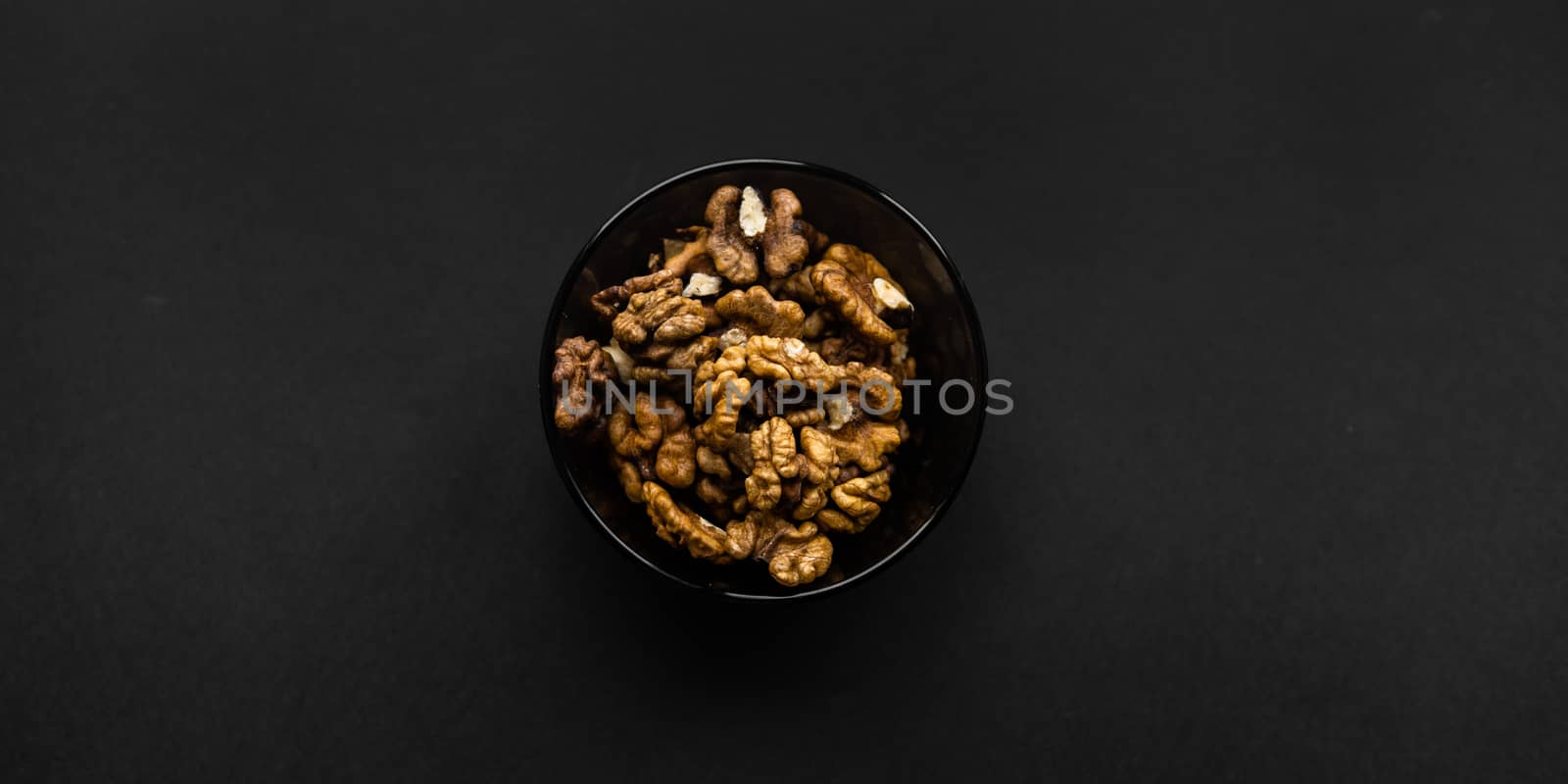 Walnut in a small plate on a black table. Walnuts is a healthy vegetarian protein nutritious food. Natural nuts snacks. by vovsht