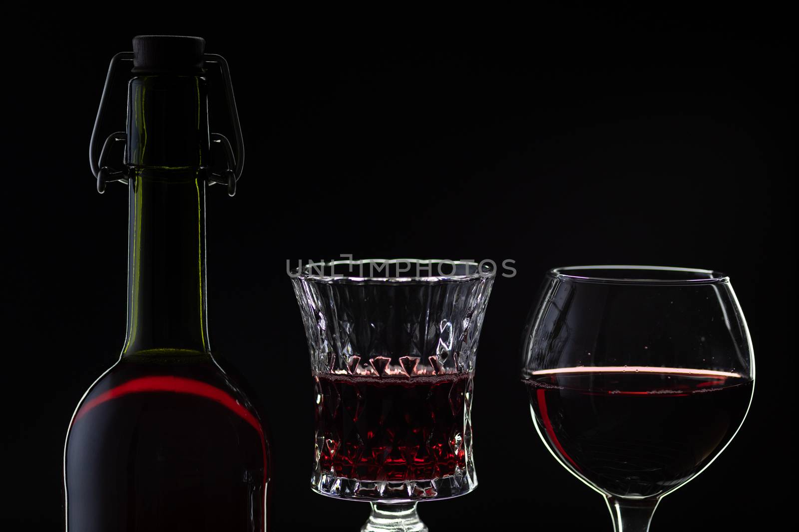 Wine. Red wine in two wine glasses over dark background. Silhouette of bottle with rose wine and opener on cork