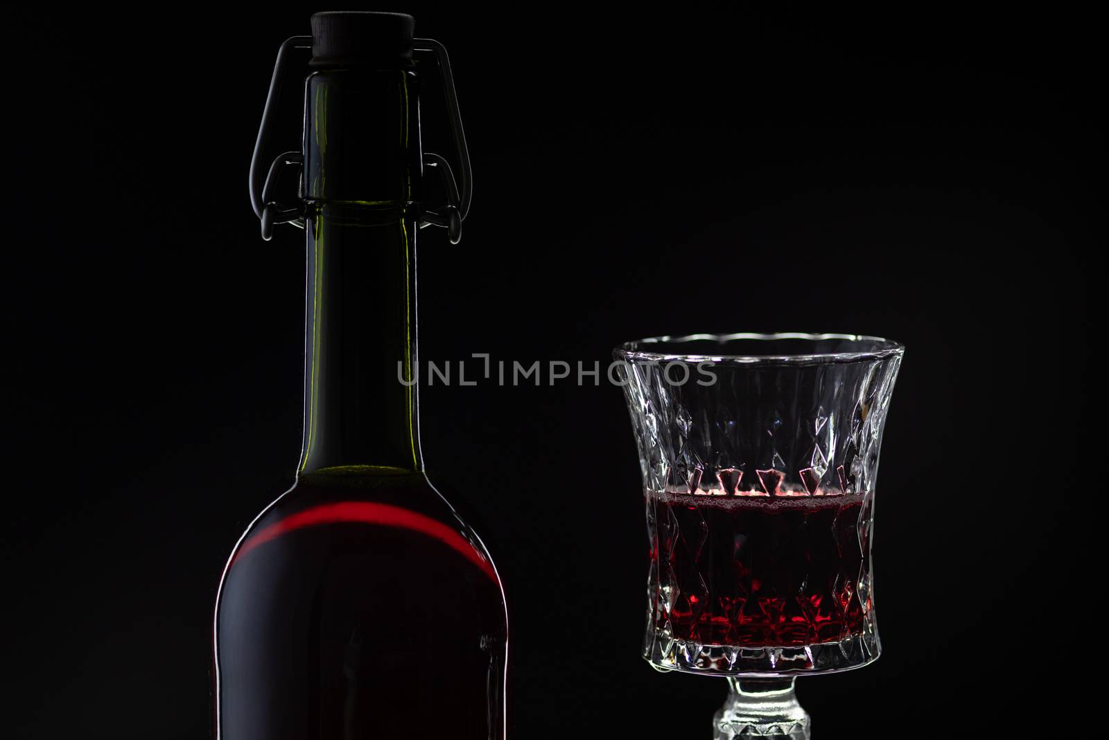 Wine. Red wine in wine glass over dark background. Silhouette of bottle with rose wine and opener on cork