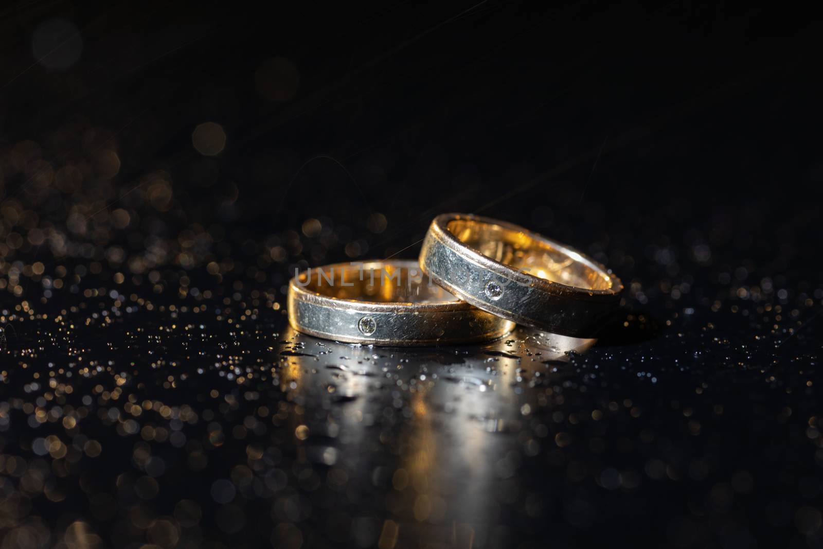 Wedding rings lying on dark surface shining with light close up macro. Water splashes