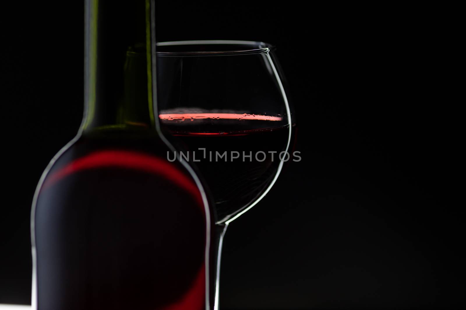 Wine. Red wine in wine glass over dark background. Silhouette of bottle with rose wine