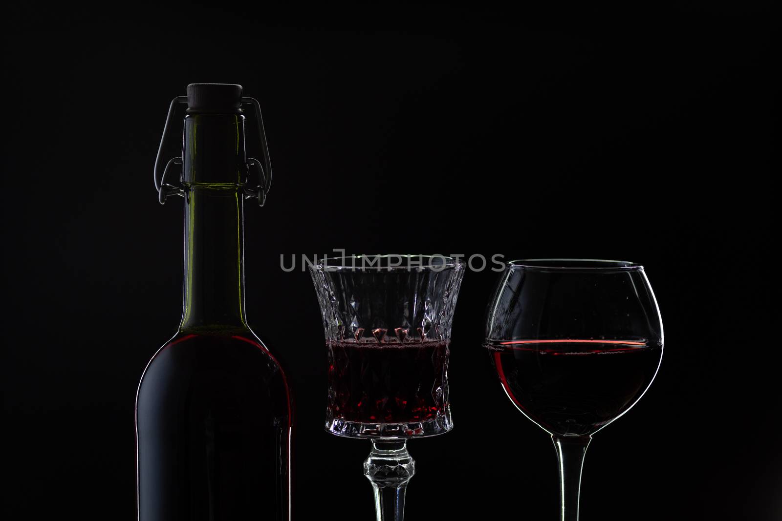 Wine. Red wine in two wine glasses over dark background. Silhouette of bottle with rose wine and opener on cork