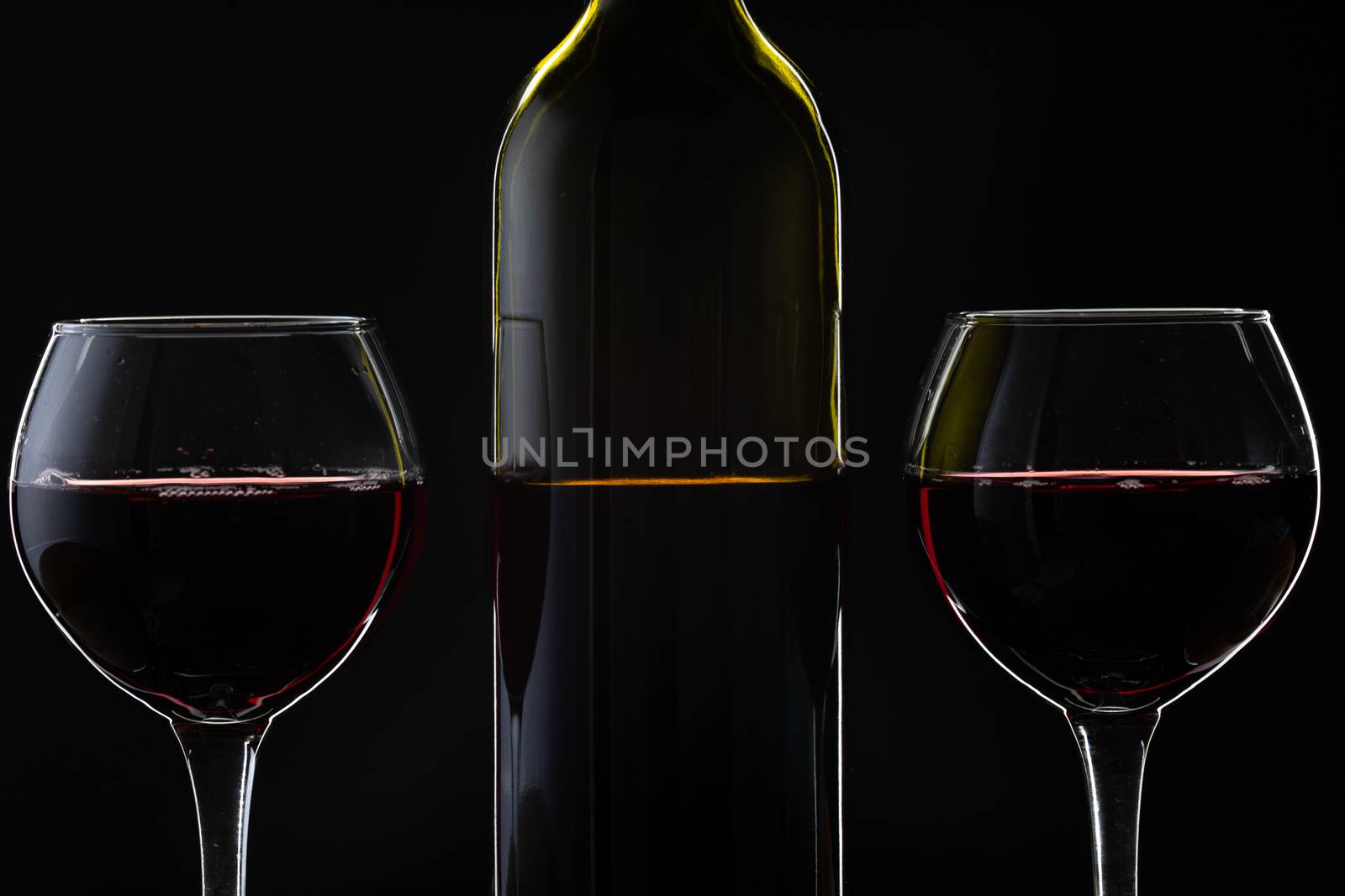 Wine. Red wine in two wine glasses over dark background. Silhouette of bottle with rose wine