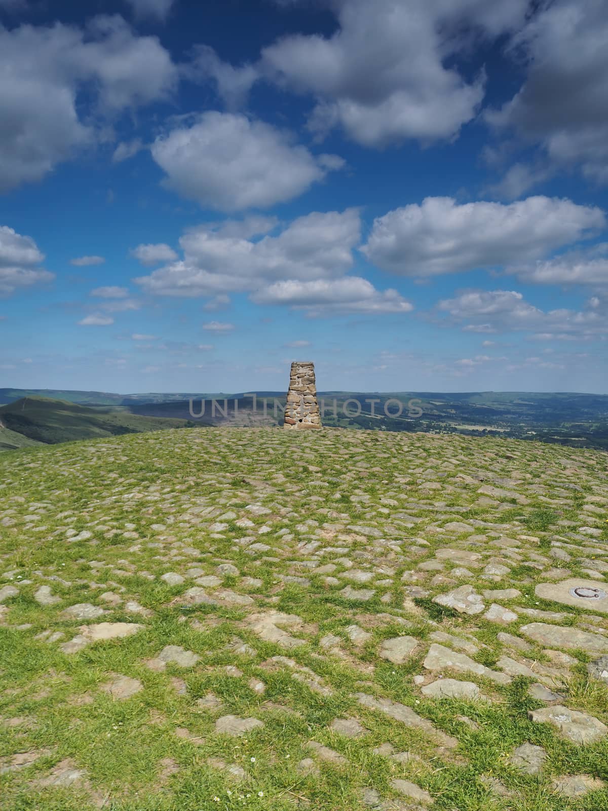Triangulation point at the top of Mam Tor overlooking the Edale valley with white clouds overhead against a blue sky, Peak District National Park, UK