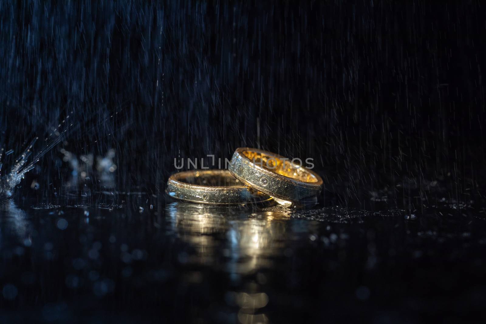 Wedding rings lying on dark surface shining with light close up macro. Water splashes