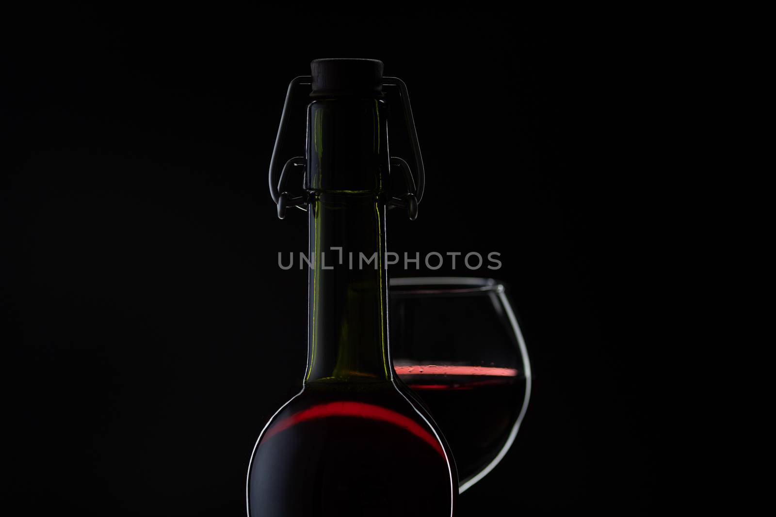 Wine. Red wine in wine glass over dark background. Silhouette of bottle with rose wine and opener on cork