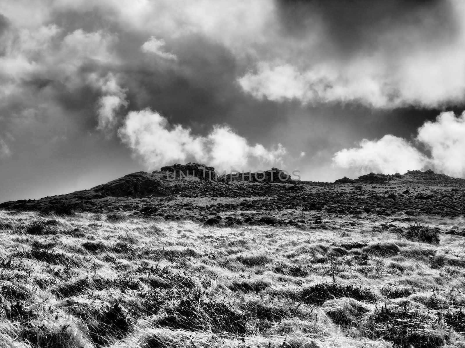 Monochrome image of rugged rocky outcrop tor on moorland hill with dark clouds rolling over, Dartmoor National Park, Devon, UK