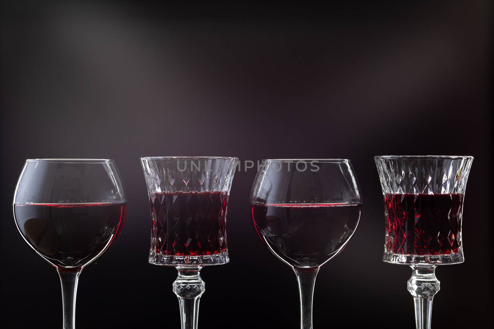 Rose wine. Red wine in four wine glasses over dark background with rays of light.