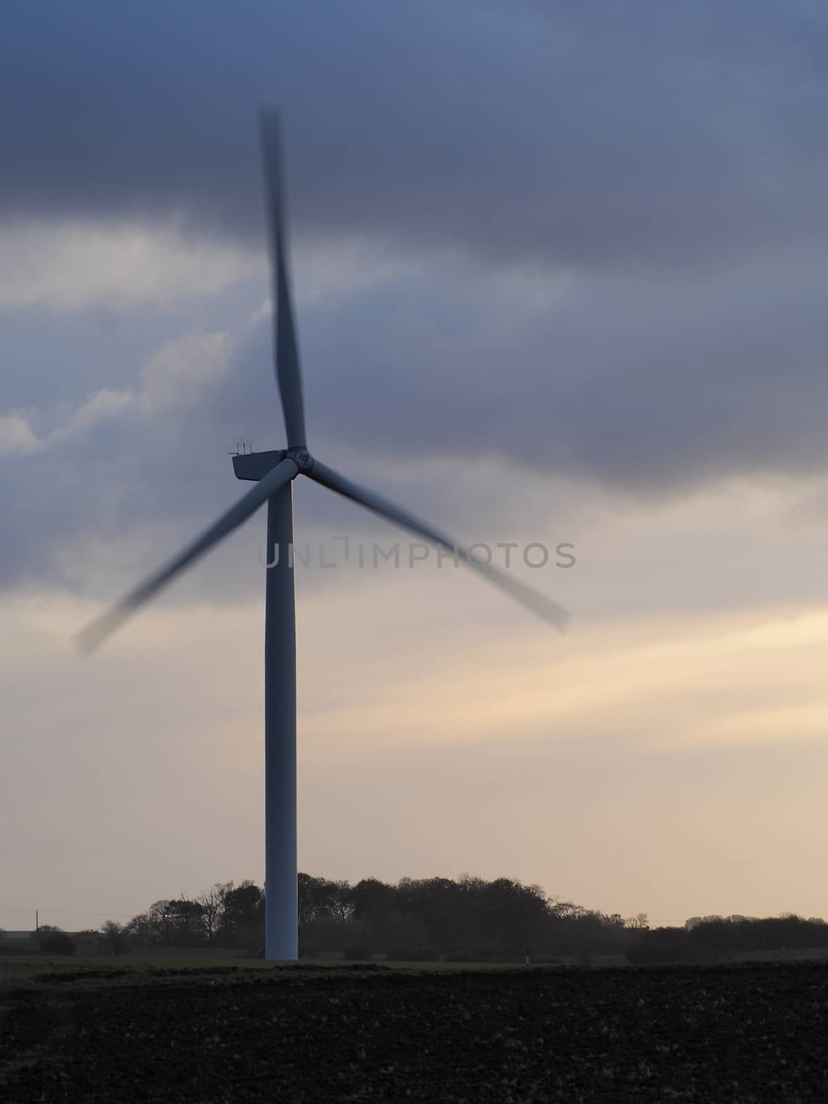 A wind turbine spinning on a windy day against a stormy and overcast evening sky by PhilHarland