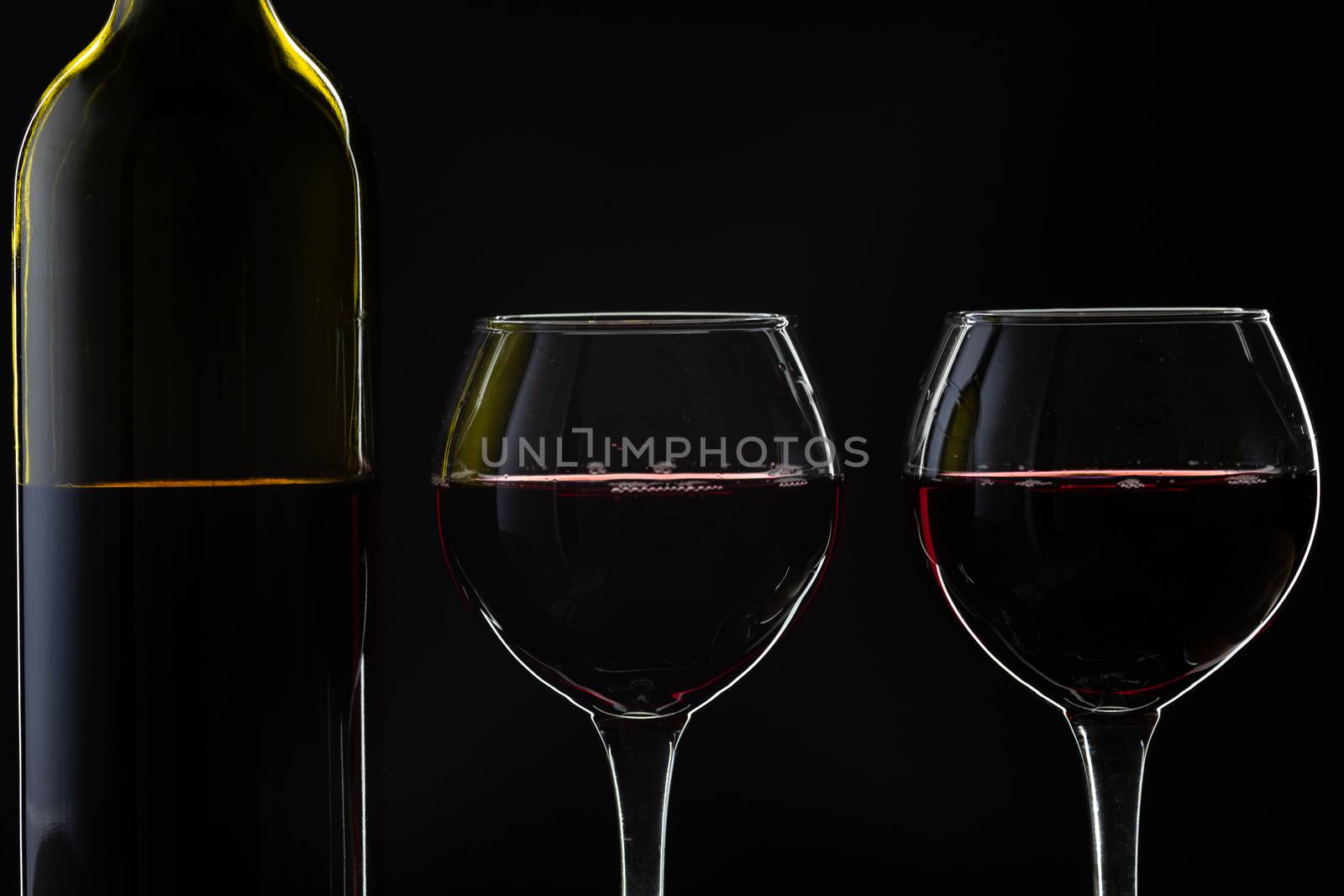 Wine. Red wine in two wine glasses over dark background. Silhouette of bottle with rose wine